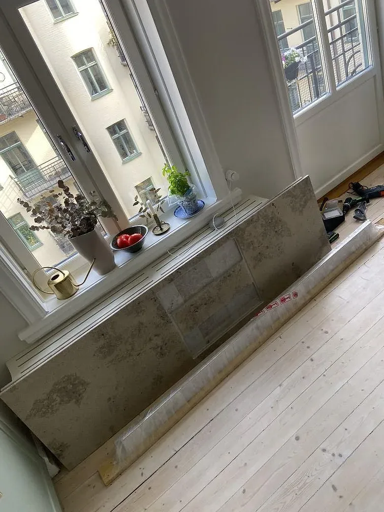 Matt köksbänkskiva i Jura Grey kalksten med fossila mönster, monterad på vita köksstommar under ett fönster i ett kök i Malmö.