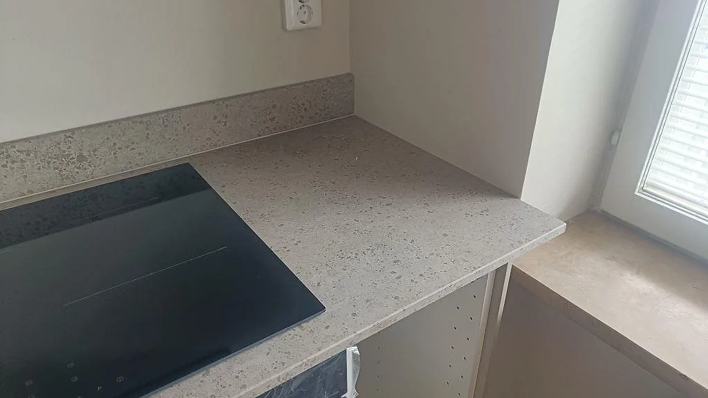Närbild av matt Jura Grey kalksten i Malmö med svart induktionshäll, uppvikt stänkkant och ljus arbetsyta vid fönster.