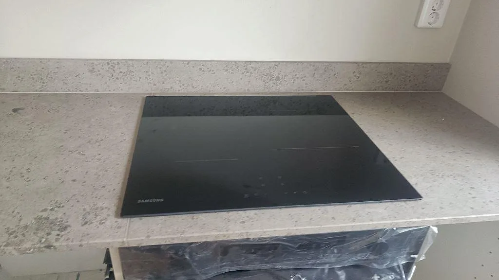 Köksbänkskiva i matt Jura Grey kalksten med svart induktionshäll och uppvikt stänkkant i ett kök i Malmö.