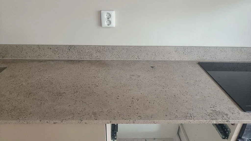Bred detalj av matt Jura Grey köksbänkskiva med uppvikt stänkkant och synlig stenstruktur intill hällen i Malmö.