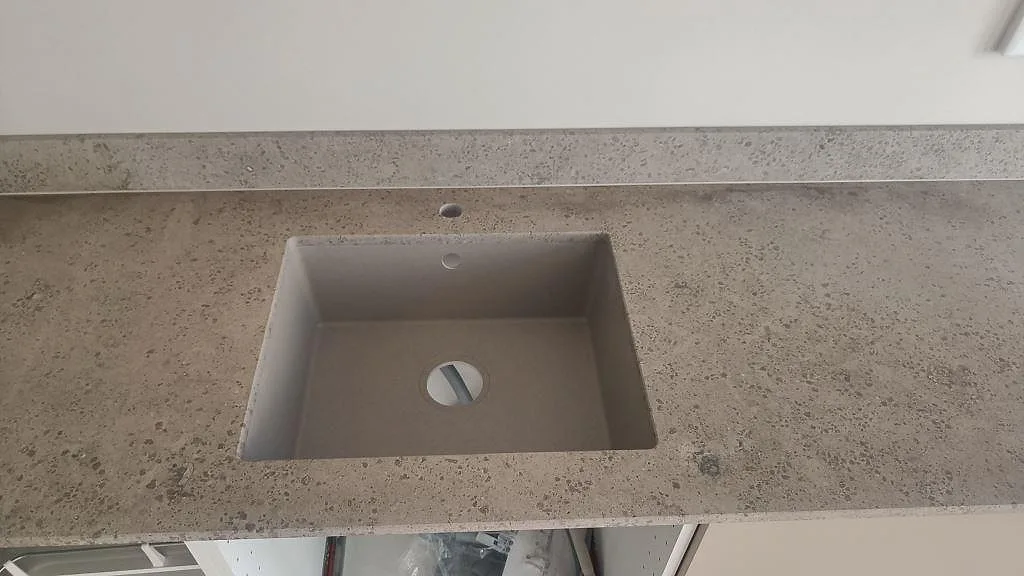 Detalj av underlimmad rostfri diskho monterad i matt Jura Grey kalksten med synlig fossilstruktur i Malmö.