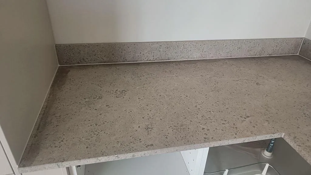 Vänster bänkrad i matt Jura Grey kalksten med uppvikt stänkkant och öppen köksstomme under montering i Malmö.