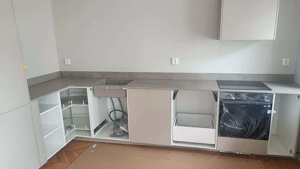 L-format kök i Malmö med matt köksbänkskiva i Jura Grey kalksten, uppvikt stänkkant, svart induktionshäll och vita stommar under montering.