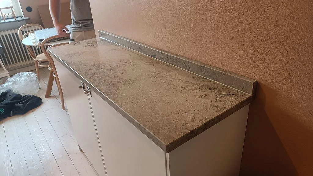 Halvö i matt Jura Grey kalksten med uppvikt stänkkant mot rosa vägg i ett kök i Malmö.