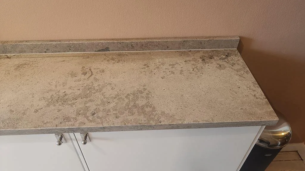 Närbild av matt Jura Grey kalksten på kökshalvö med uppvikt stänkkant och vit inredning i Malmö.