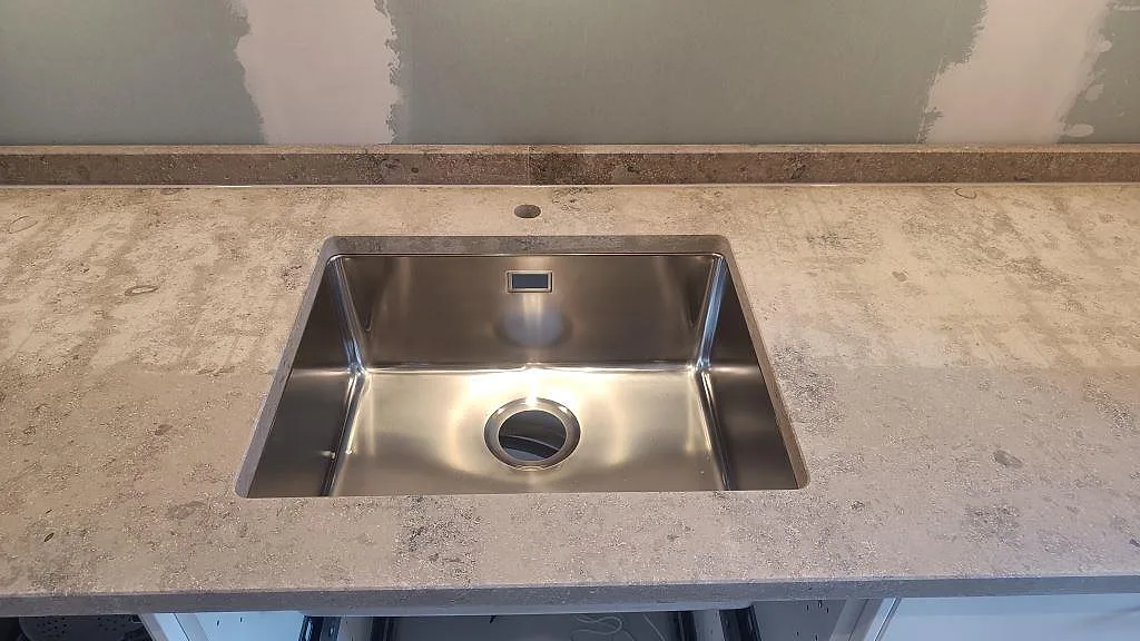 Underlimmad rostfri diskho i en matt Jura Grey köksbänkskiva med uppvikt stänkkant i ett kök i Malmö.
