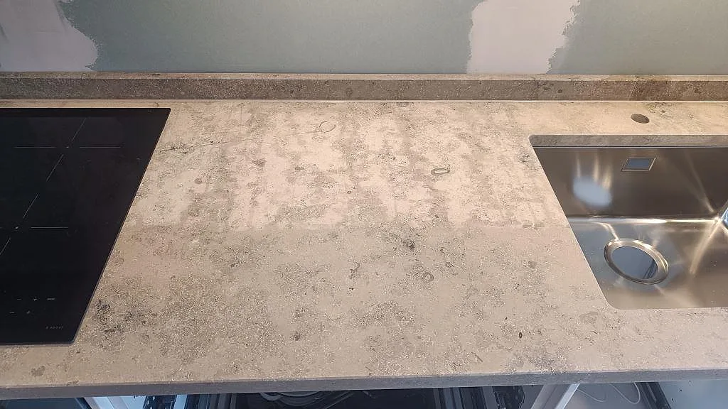 Matt köksbänkskiva i Jura Grey kalksten i Malmö med induktionshäll, underlimmad rostfri diskho och låg stänkkant längs väggen.