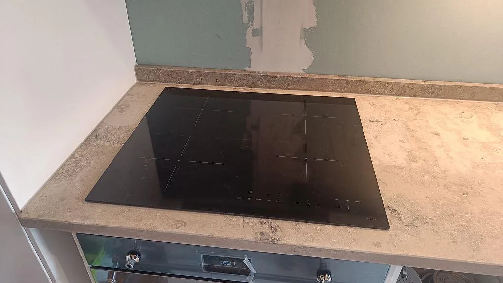 Induktionshäll monterad i matt Jura Grey kalksten med låg stänkkant och vit köksinredning i Malmö.