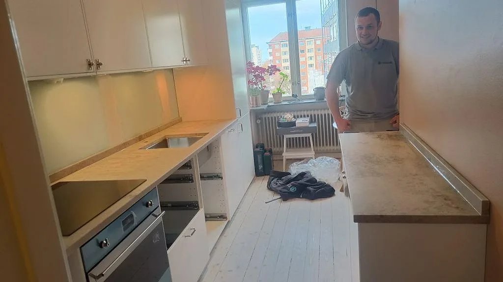 L-format kök i Malmö med matt köksbänkskiva i Jura Grey kalksten, underlimmad rostfri diskho, induktionshäll och halvö vid rosa vägg.
