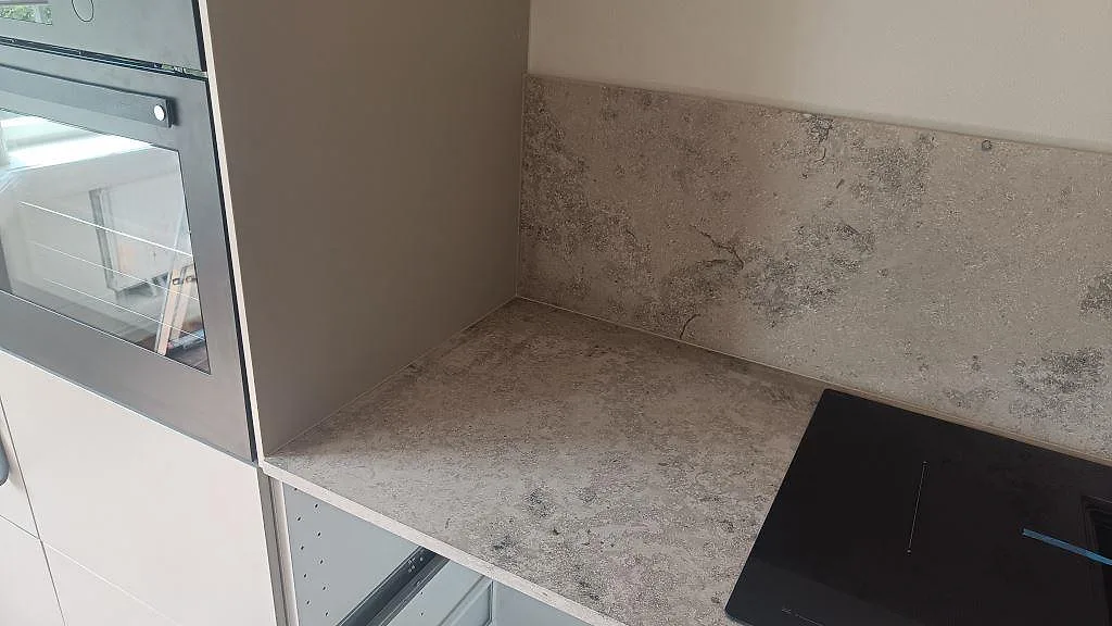 Köksbänkskiva i matt Jura Grey kalksten med stänkskydd och svart häll i ett kök i Malmö.