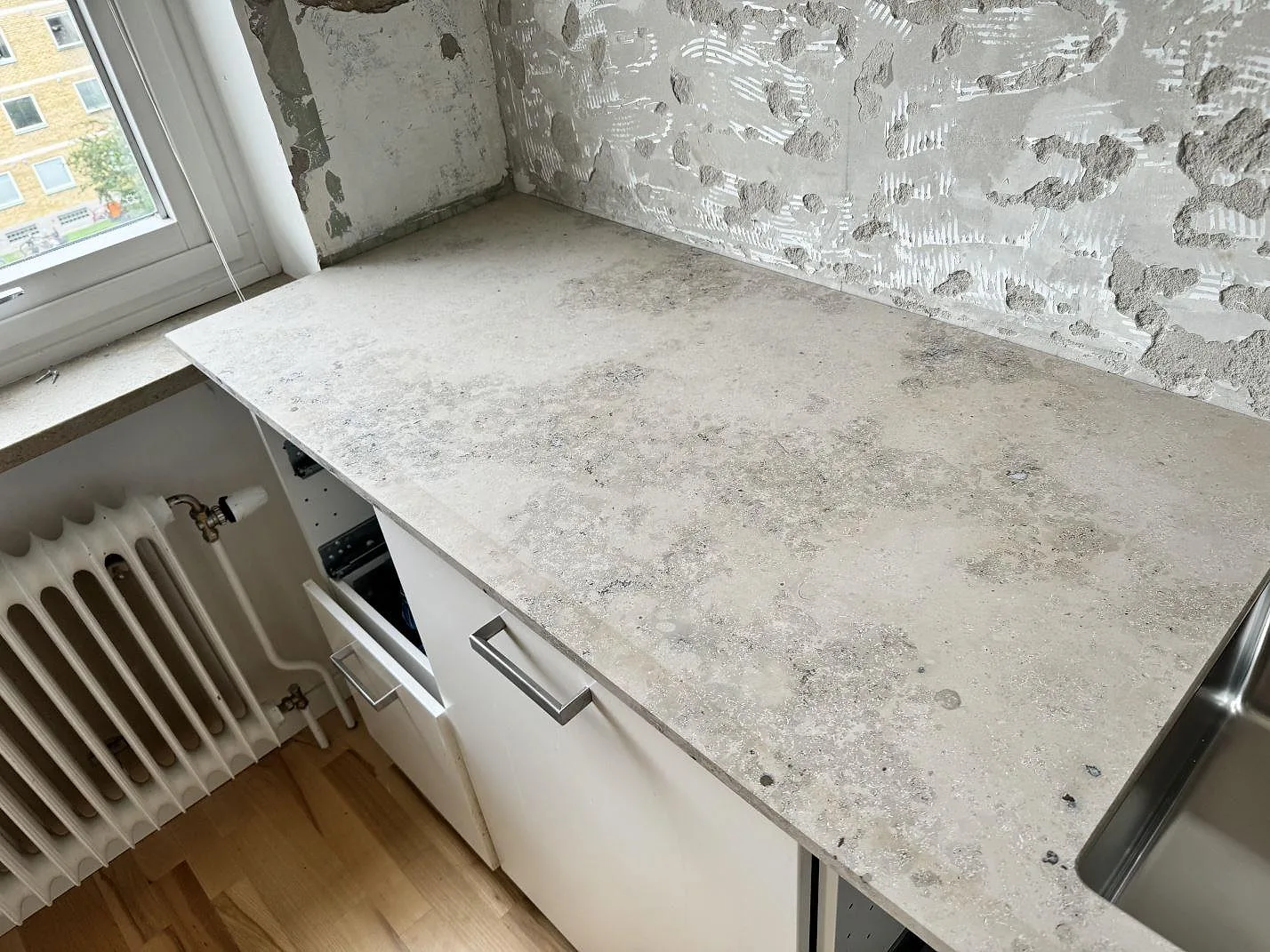 Matt Jura Grey bänkskiva vid fönster och radiator, med grå kalksten och synlig diskho i ett kök i Malmö.