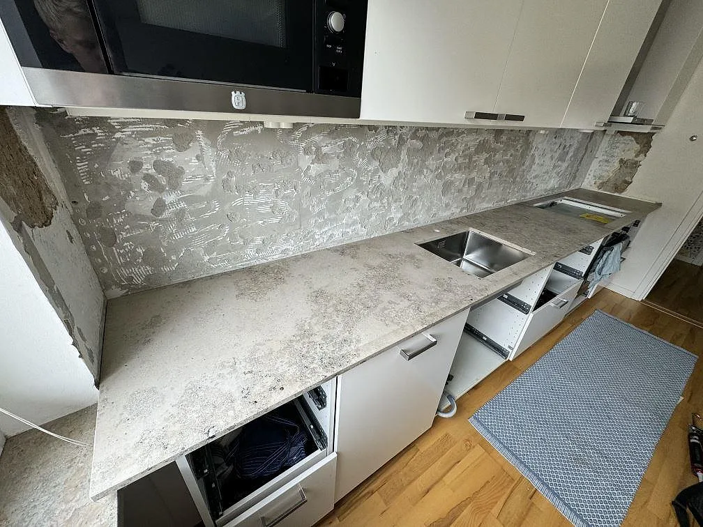 Köksbänkskiva i matt Jura Grey, grå kalksten, monterad längs en köksvägg med rostfri diskho och öppna stommar i Malmö.