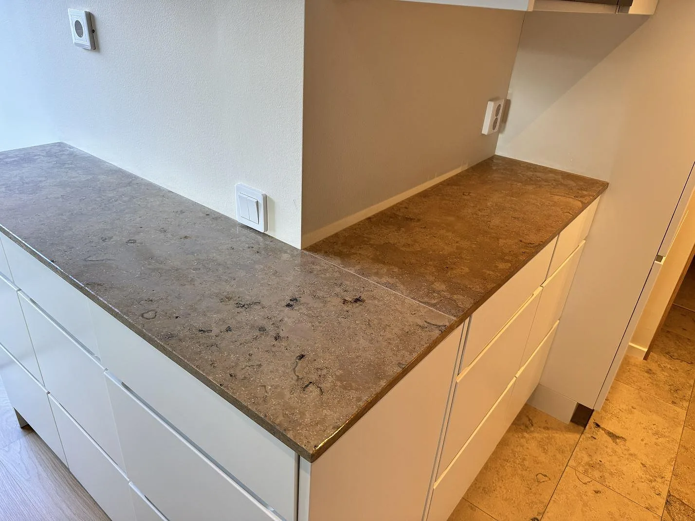Vinkelvy av köksbänkskiva i matt Jura Grey kalksten med grå fossilteckning över vita lådor i Malmö.