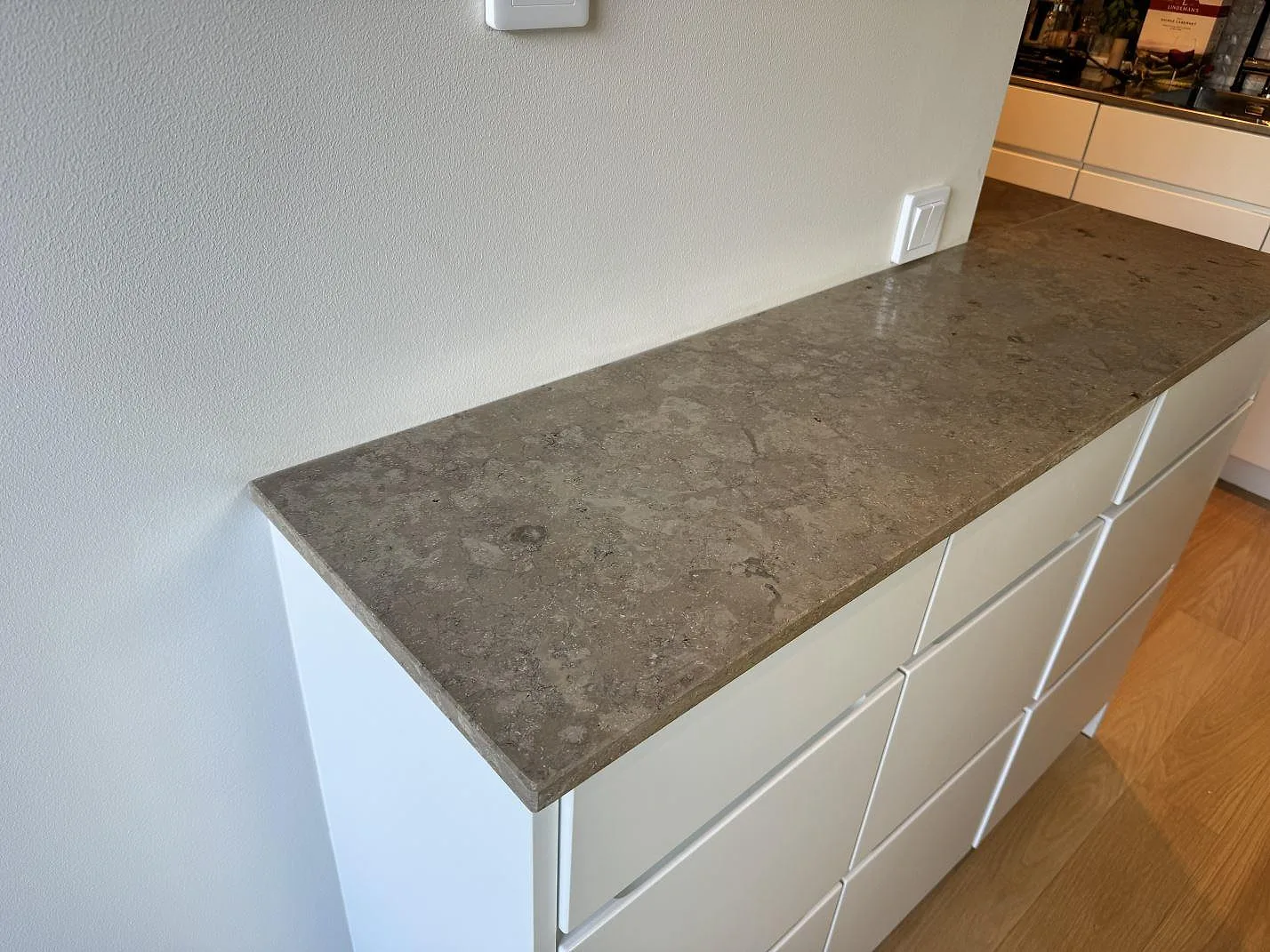 Rak vy över köksbänkskiva i matt Jura Grey kalksten med grå ådring på vit skåprad i Malmö.