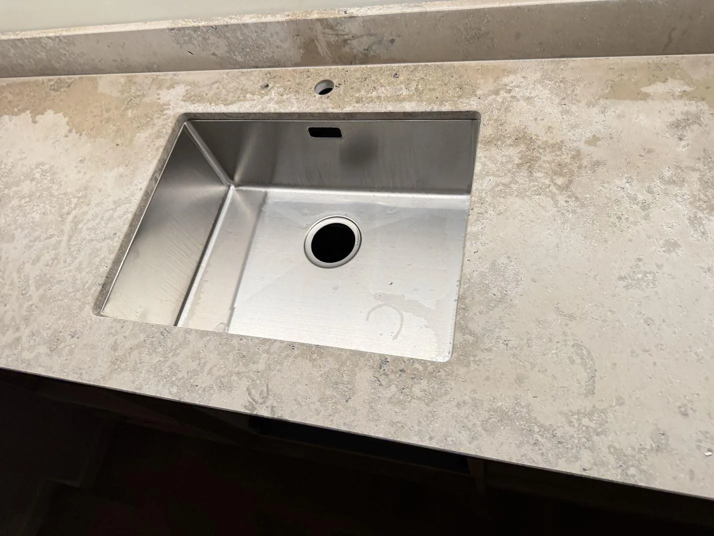 Närbild av rostfri diskho i en matt Jura Grey bänkskiva med naturlig fossilstruktur i Malmö.