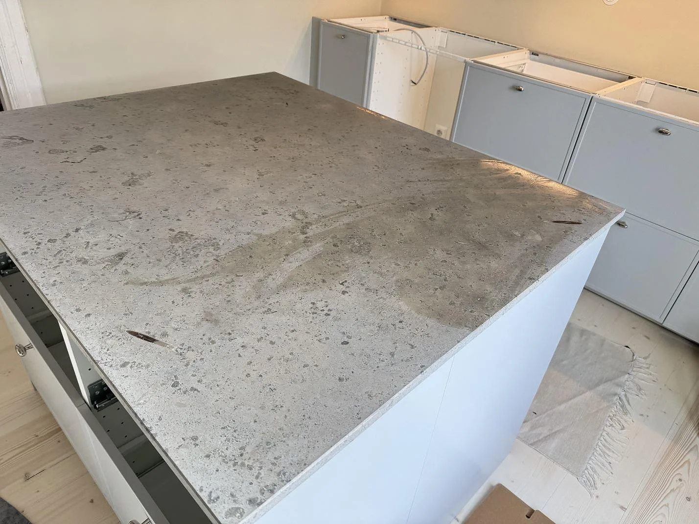 Köksbänkskiva i Jura Grey, matt naturlig kalksten, på en köksö med molnig grå ådring i ett kök under montering i Malmö.