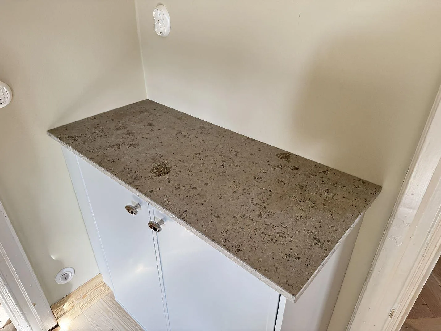 Smalare bänkskiva i matt Jura Grey kalksten med tydlig fossilstruktur på ett vitt underskåp i en nisch i Malmö.