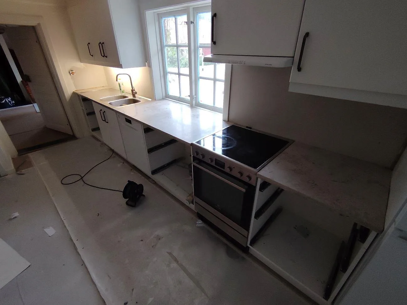 Köksbänkskiva i matt Jura Grey kalksten, 30 mm, längs en rak köksrad med diskho, spis och fönster i Mariefred.