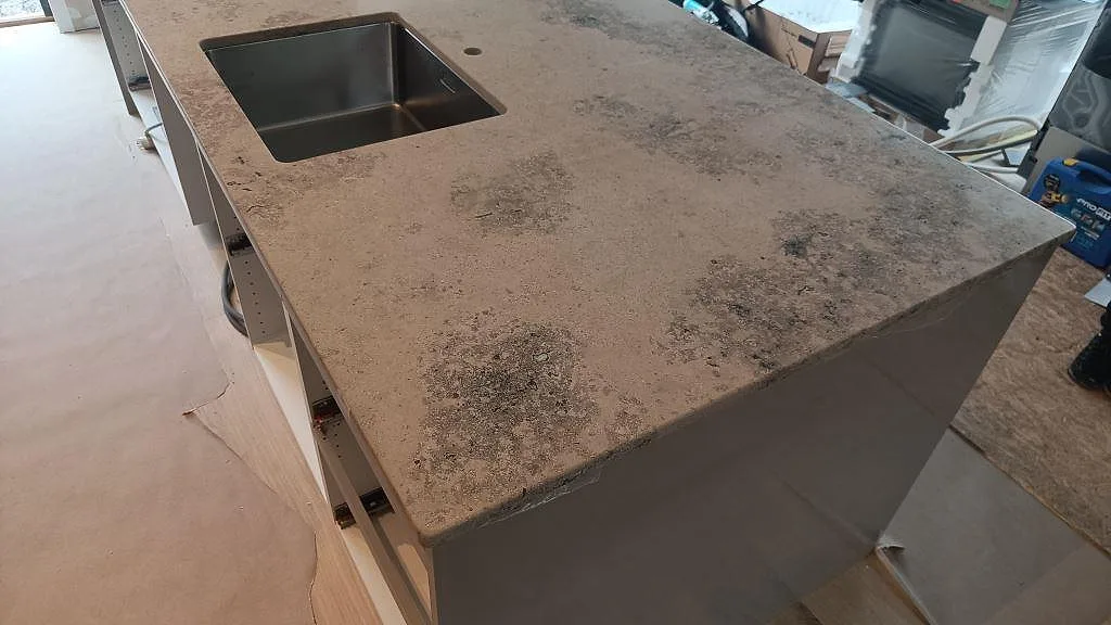 Köksö med matt Jura Grey bänkskiva där diskhon syns i stenytan under montering i Marstrand.