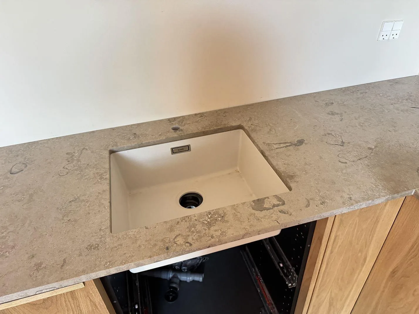 Underlimmad ljus diskho i en matt Jura Grey köksbänk i kalksten med blandarhål i ett kök i Nivå.