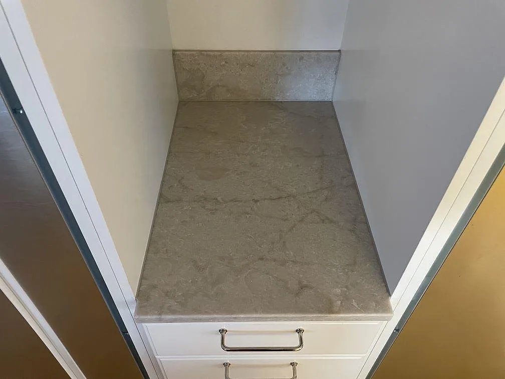 Mindre bänkskiva i matt Jura Grey kalksten i en nisch med stänkskydd och vita lådfronter, med synliga fossilspår och mjuk ådring, i ett kök i Nykvarn.