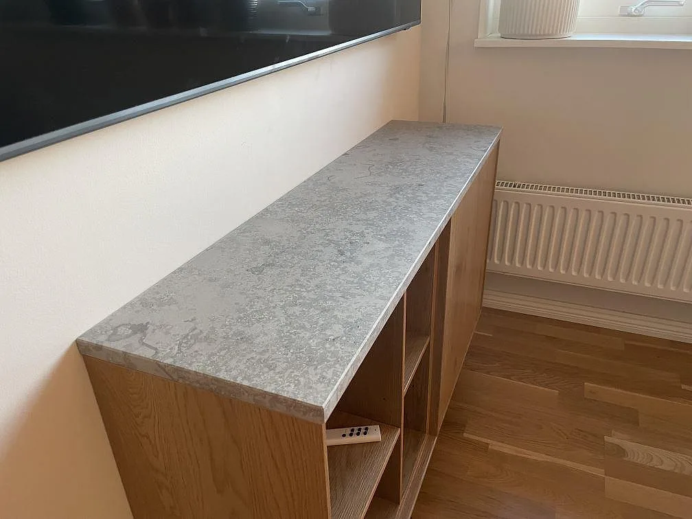 Köksbänkskiva i matt Jura Grey kalksten monterad ovanpå en öppen ekstomme med uppvikt stänkkant i samma sten, i ett kök i Nykvarn.