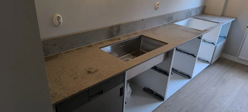 Köksbänkskiva i matt Jura Grey med rostfri diskho och uppvikt stänkkant längs öppna köksstommar i Oxelösund.