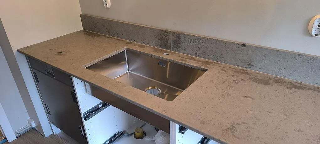 Detalj av matt Jura Grey köksbänkskiva med rostfri diskho och grå stänkkant i ett kök i Oxelösund.
