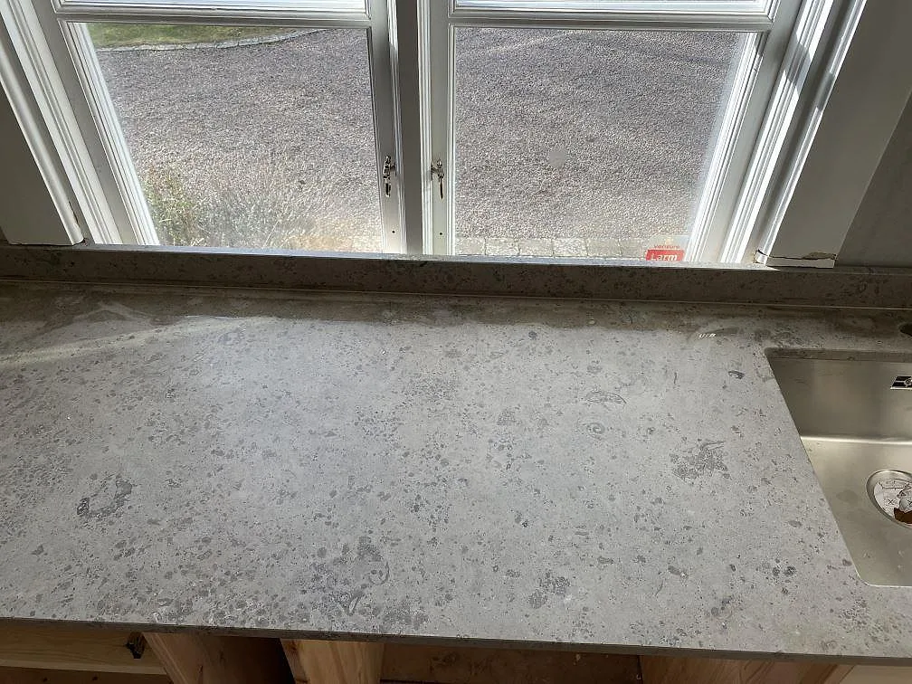 Matt Jura Grey köksbänkskiva under fönster med grå ådring och uppvikt stänkkant i Ronneby.