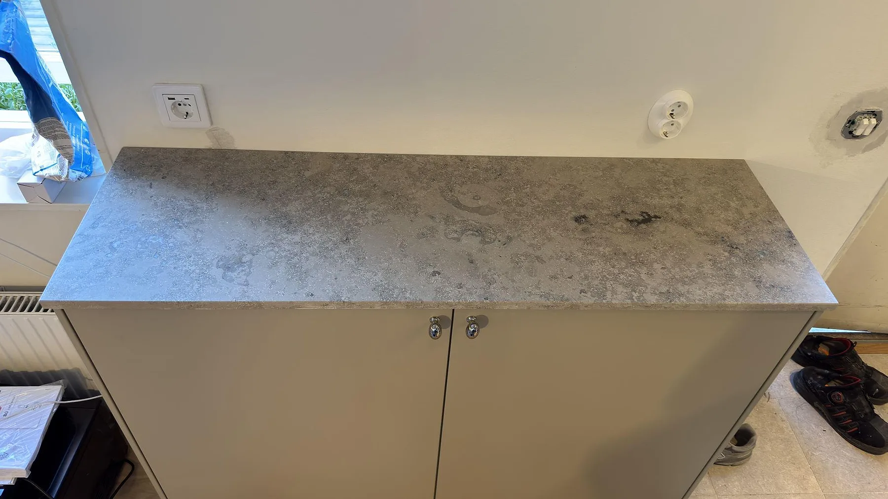 Mindre bänkskiva i matt Jura Grey kalksten på skåp vid fönster i Saltsjö Boo, med fossil och grå stenstruktur synlig.