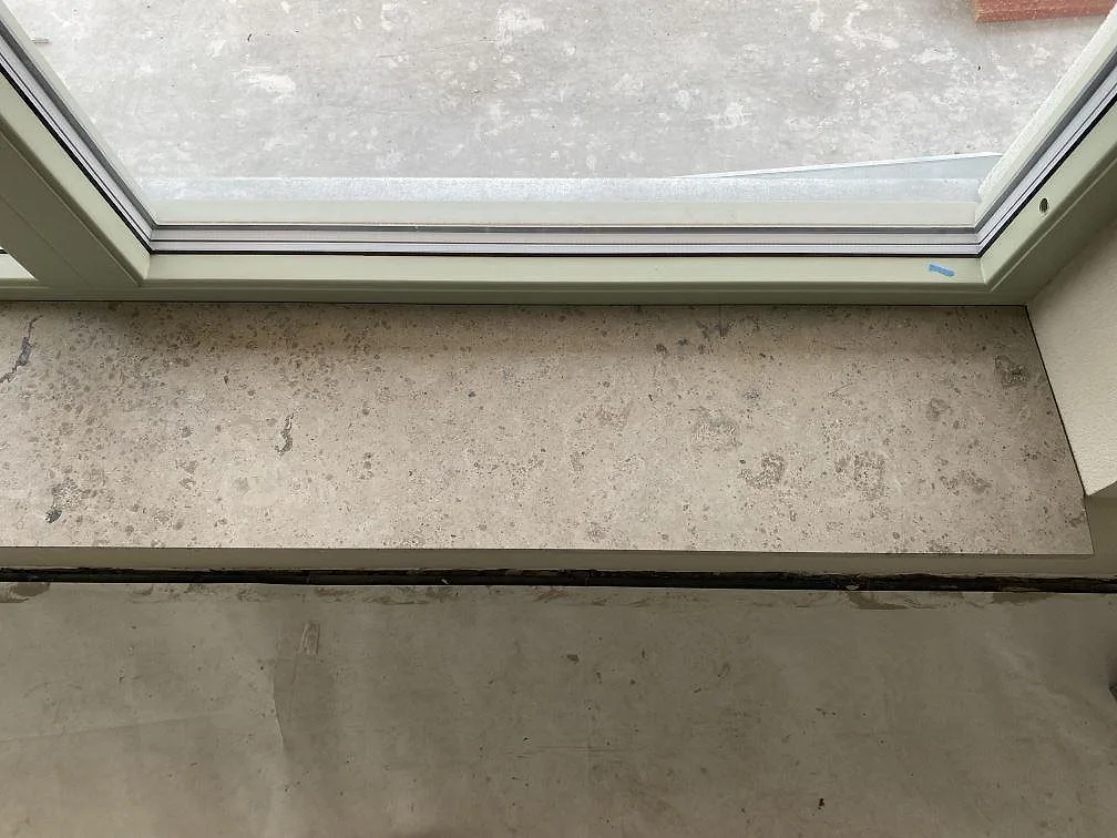 Detalj av fönsterbänk i matt Jura Grey kalksten med fossilrik grå yta vid fönsterkarm i Sankt Olof.