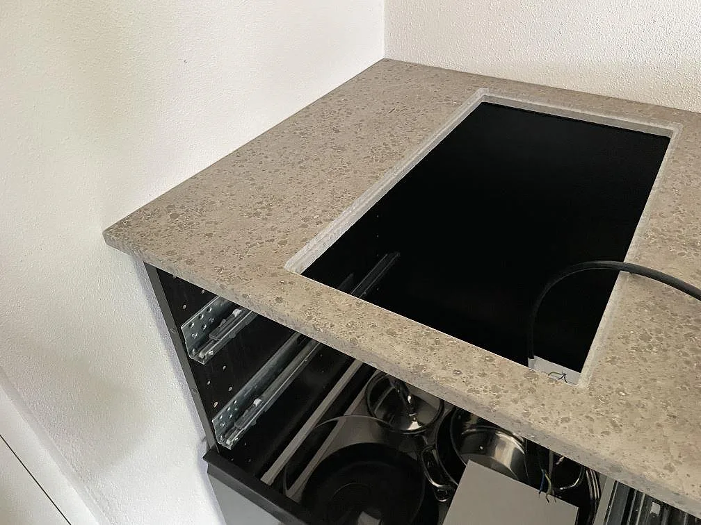Detalj av hällurtag i matt Jura Grey kalksten, 20 mm köksbänkskiva, med öppna skåp i Skanör.