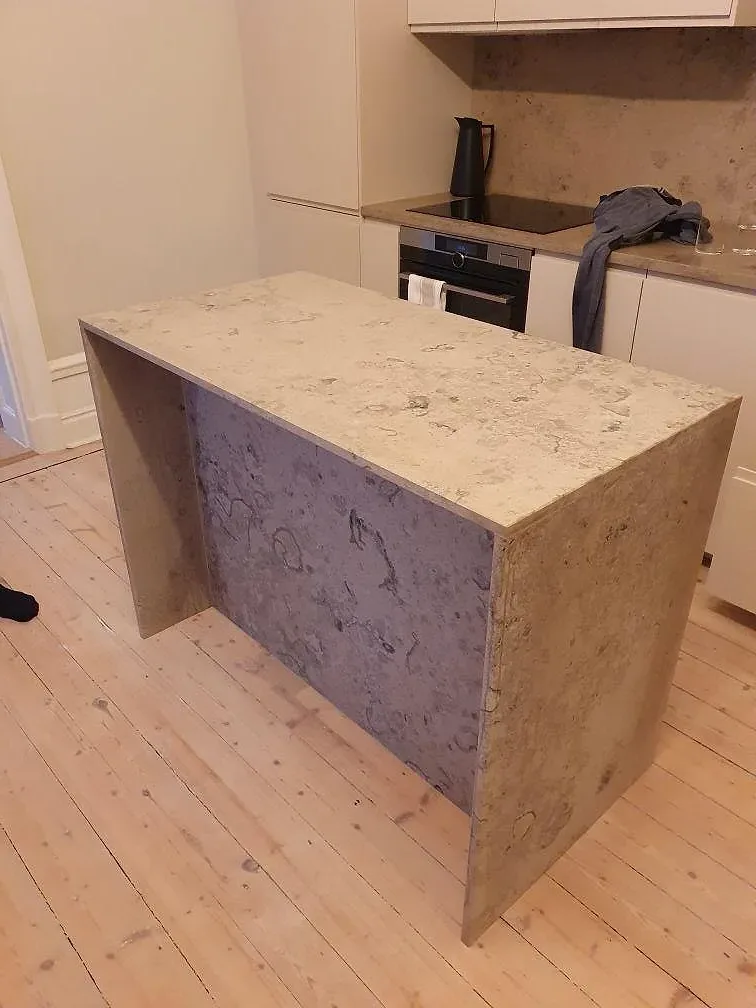 Sidovy av köksö i matt Jura Grey med stenklädd front och ljus köksinredning under montering i Stockholm.
