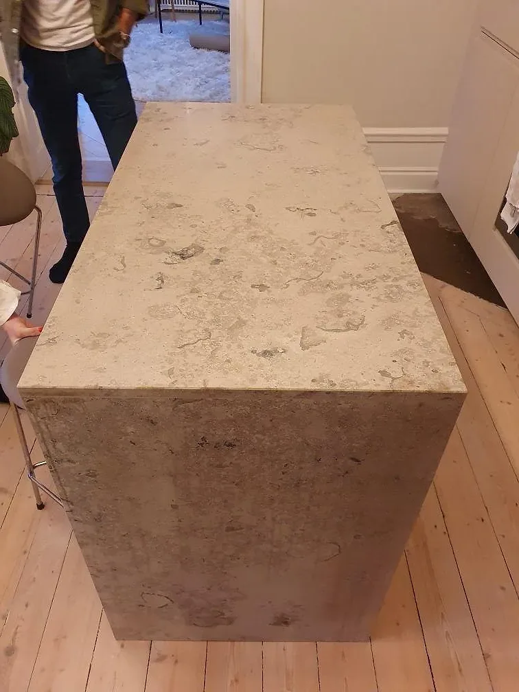 Närbild på köksö i matt Jura Grey med stenklädd front och gavel i ett kök med trägolv i Stockholm.