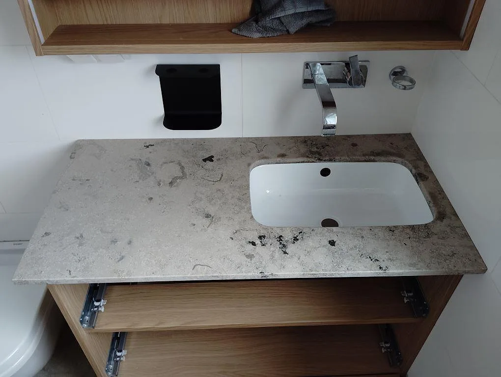 Badrumsbänkskiva i matt Jura Grey kalksten över träinredning med vitt tvättställ och tydlig fossilådring i Stockholm.