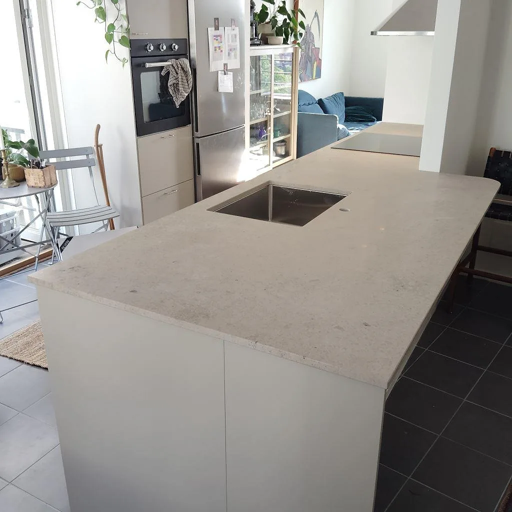 Matt köksbänkskiva i Jura Grey på en vit kökshalvö i ett öppet kök i Stockholm, med ljus stenyta och mörkt klinkergolv.