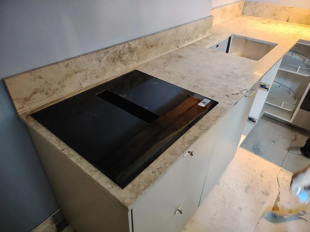 Detalj av matt Jura Grey köksbänkskiva i kalksten med häll, diskho och uppvikt stänkskydd under montering i Stockholm.