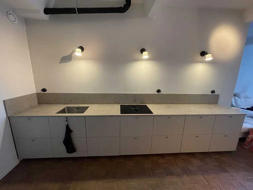 Rak köksbänkskiva i matt Jura Grey kalksten med stänkkant under vägglampor i ett kök i Stockholm.