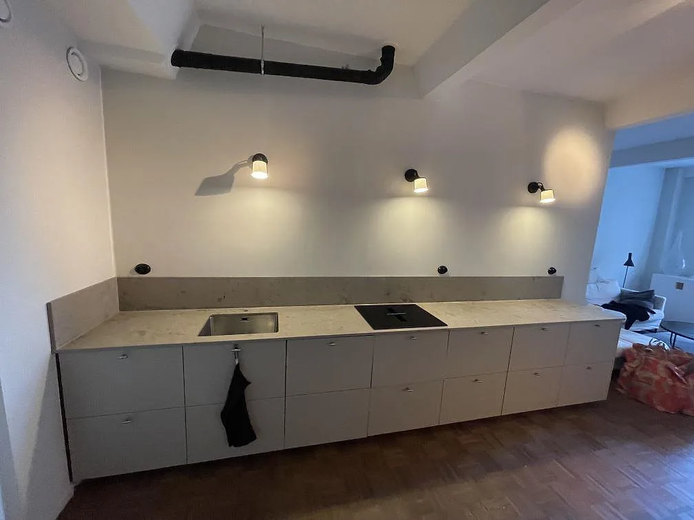 Bred vy över kök i Stockholm med matt Jura Grey bänkskiva och låg stänkkant under montering.