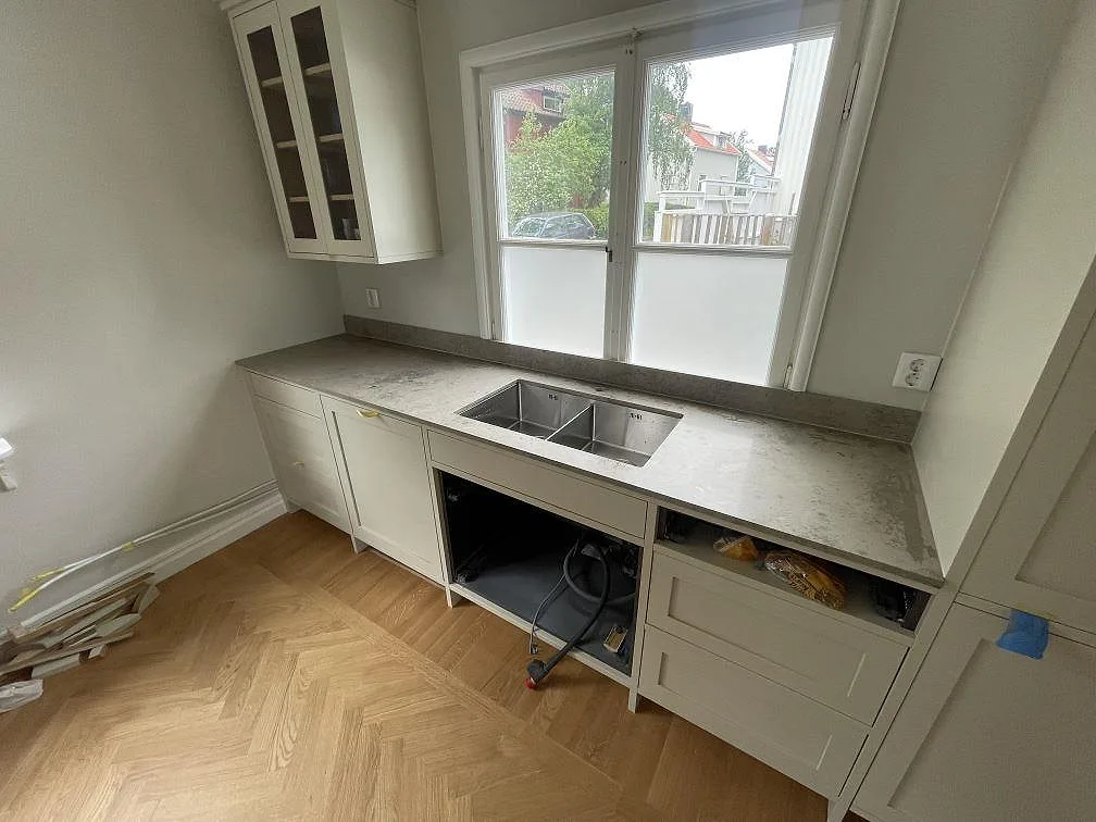 Lång diskbänksdel i matt Jura Grey kalksten med diskho, skåpstommar och stänkkant under fönster i Stockholm.