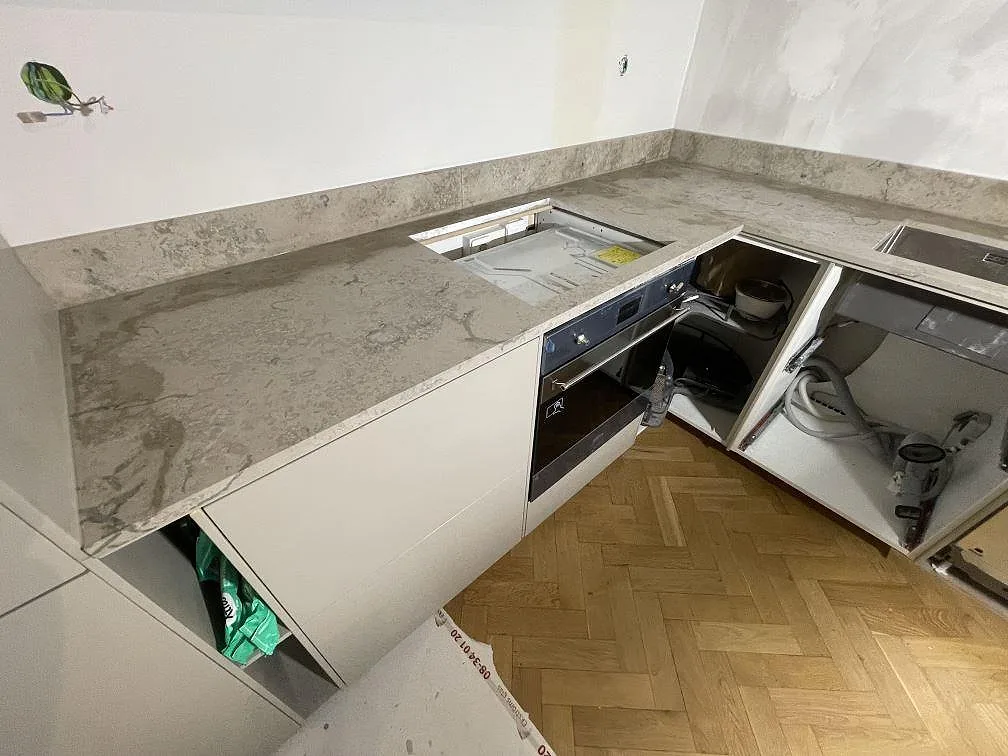 Bänkskiva i matt Jura Grey kalksten med hällurfräsning och molnig grå ådring i ett kök under montering i Stockholm.