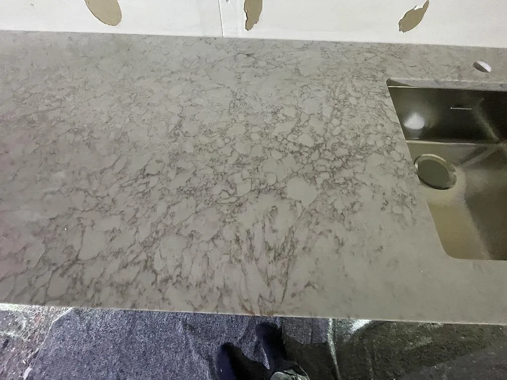 Närbild på den matta Jura Grey-skivans ådring med underlimmad rostfri diskho, kalksten i ett kök i Stockholm.
