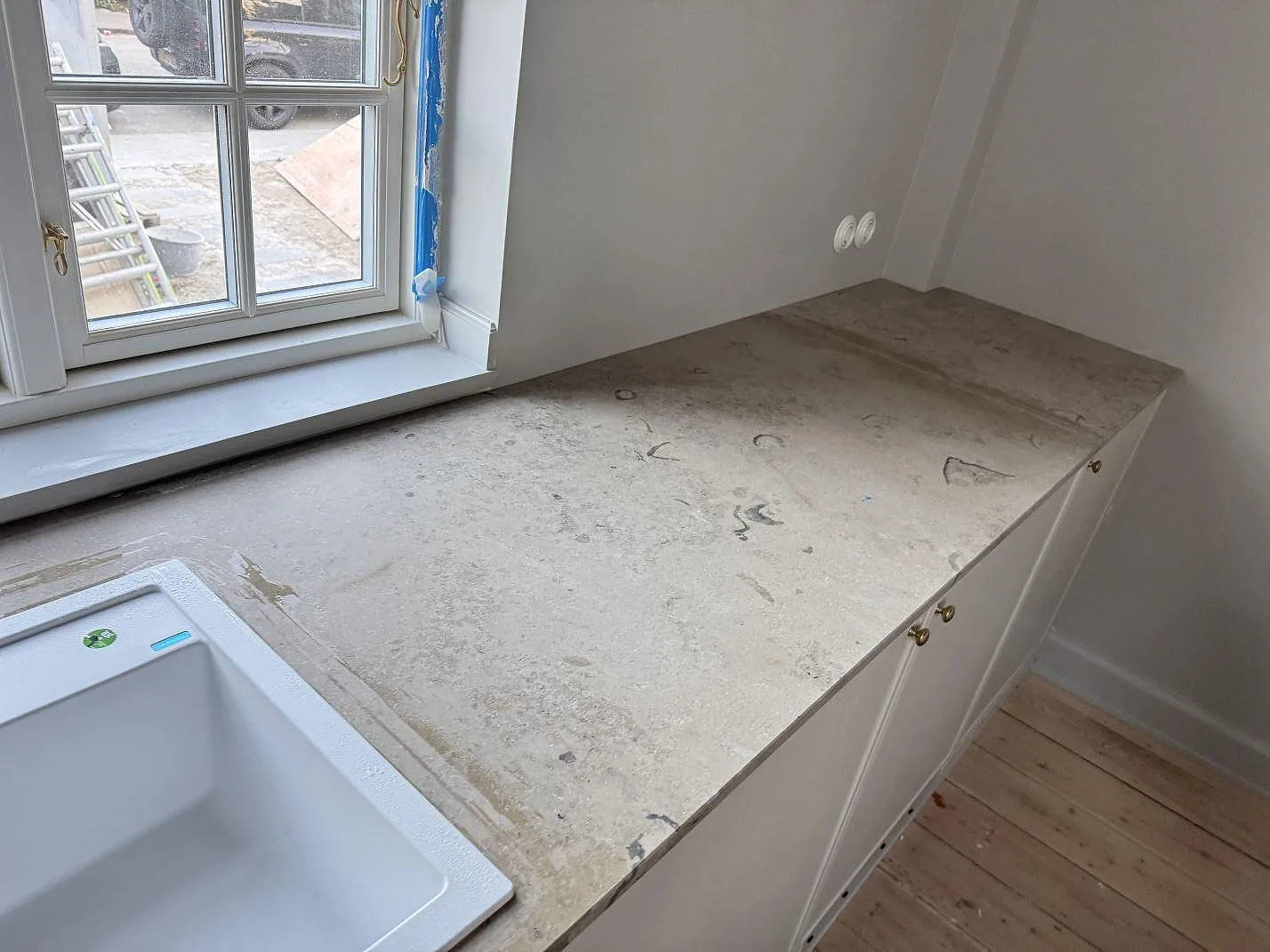 Lång bänkrad i matt Jura Grey kalksten under fönster, monterad på ljus köksinredning i Stueetagen Sorø.