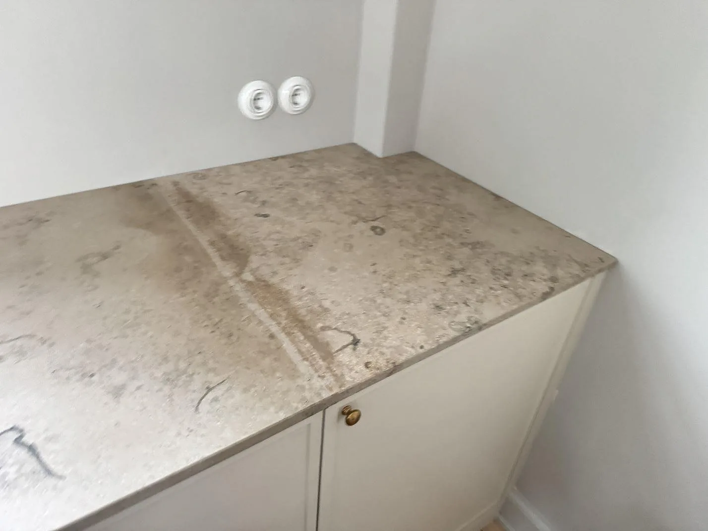 Hörnvy av matt Jura Grey bänkskiva med tydliga fossilmönster mot ljusa skåp i Stueetagen Sorø.