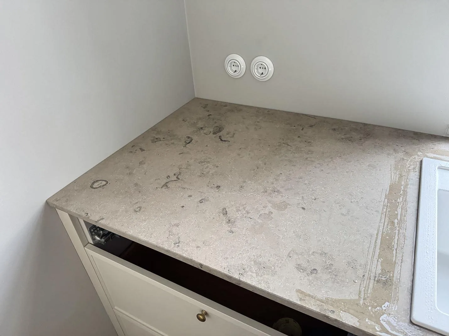 Närbild av matt köksbänkskiva i Jura Grey med gråbeige fossilstruktur och vägguttag i Stueetagen Sorø.