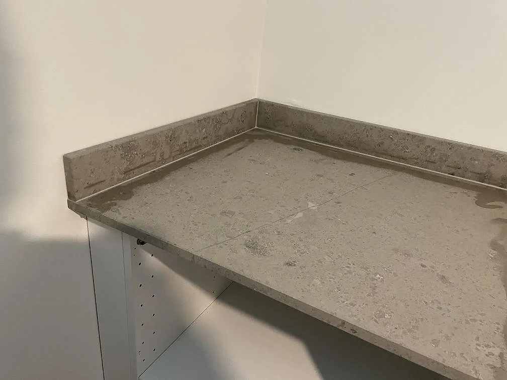 Hörn av bänkskiva i matt Jura Grey kalksten med gråbeige ådring och uppvikt stänkkant i Töllsjö.