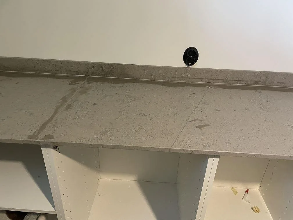 Lång arbetsbänk i matt Jura Grey kalksten över vita skåpstommar med uppvikt stänkkant i Töllsjö.