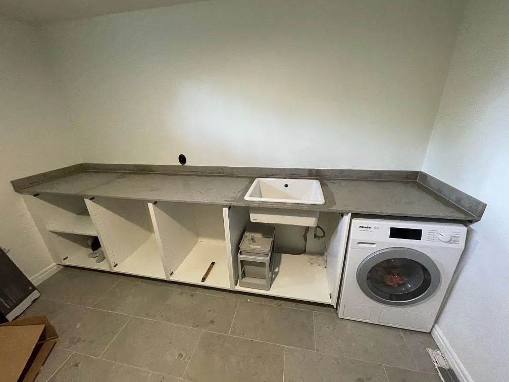 Bänkskiva i matt Jura Grey kalksten med vit övermonterad tvättho och Miele tvättmaskin i en tvättstuga i Töllsjö.