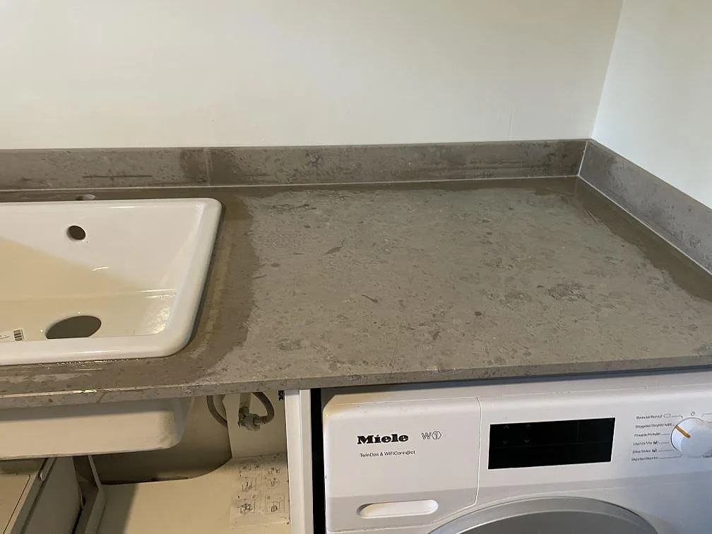 Arbetsbänk i matt Jura Grey kalksten med vit tvättho och tvättmaskin under skivan i Töllsjö.