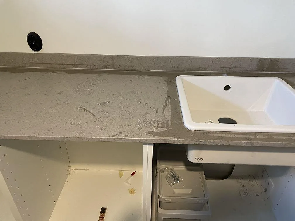 Närbild på matt Jura Grey kalksten med uppvikt stänkkant och vit övermonterad tvättho i en tvättstuga i Töllsjö.